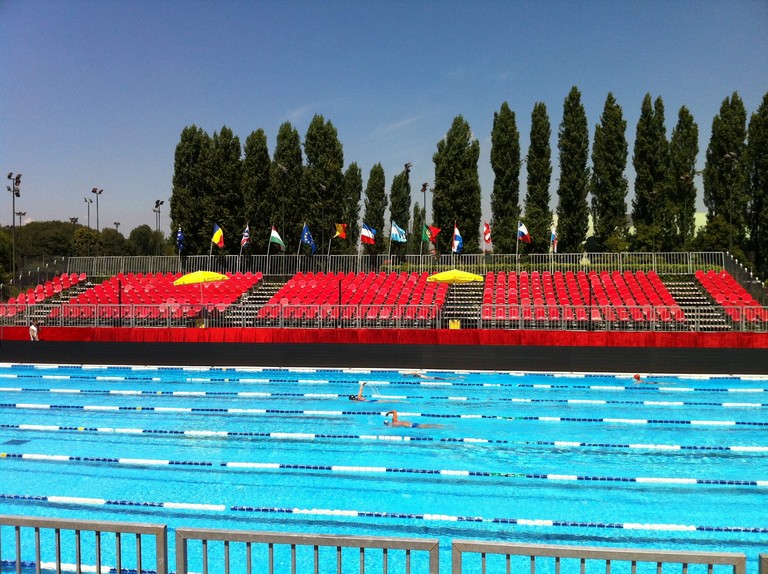 Tribune con sedute rosse a bordo di una piscina, con bandiere sullo sfondo