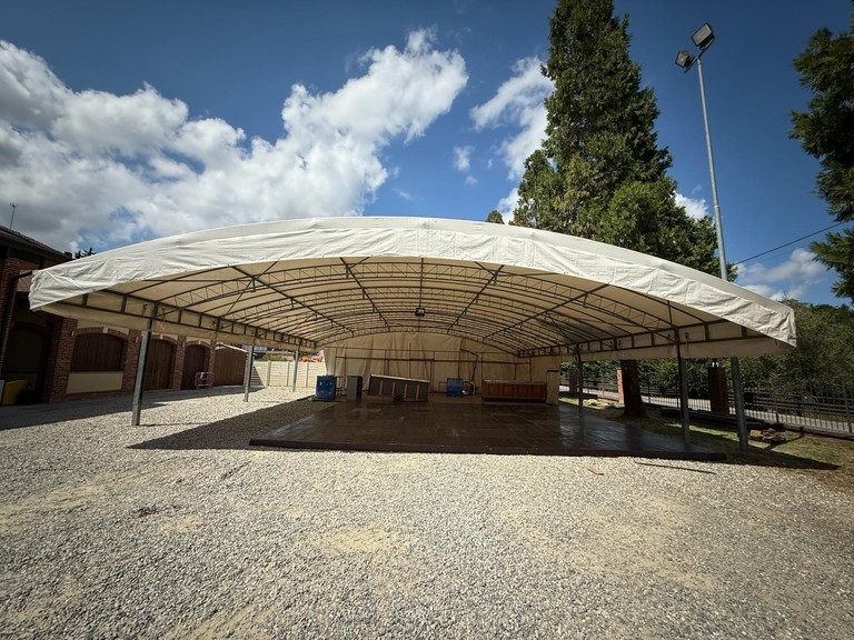 Copertura ad arco con telo bianco montata su un piazzale tra gli alberi